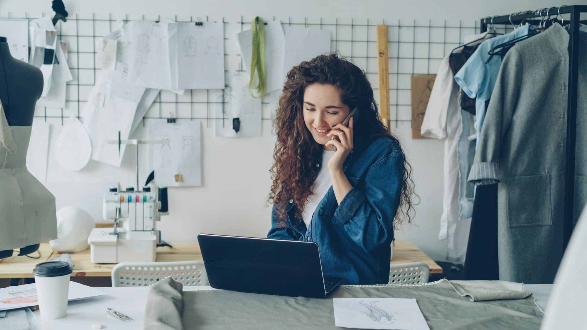 A small business owner on the phone while working on a laptop in her studio